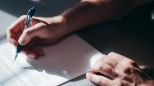 Zbliżenie na dłoń piszącą piórem na białym papierze – profesjonalne tworzenie CV i doradztwo kariery na cvsearch.pl