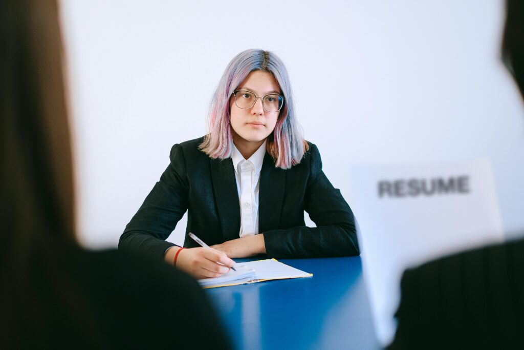 Młoda kobieta z fioletowymi włosami w czarnym żakiecie podczas rozmowy kwalifikacyjnej przed dokumentem "Resume" – profesjonalna rekrutacja i doradztwo kariery na cvsearch.pl